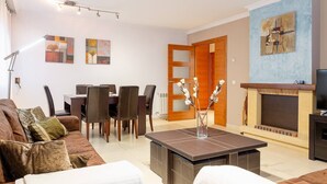 A living room with a sofa, coffee table, and a fireplace. There is a dining area with chairs and a table.