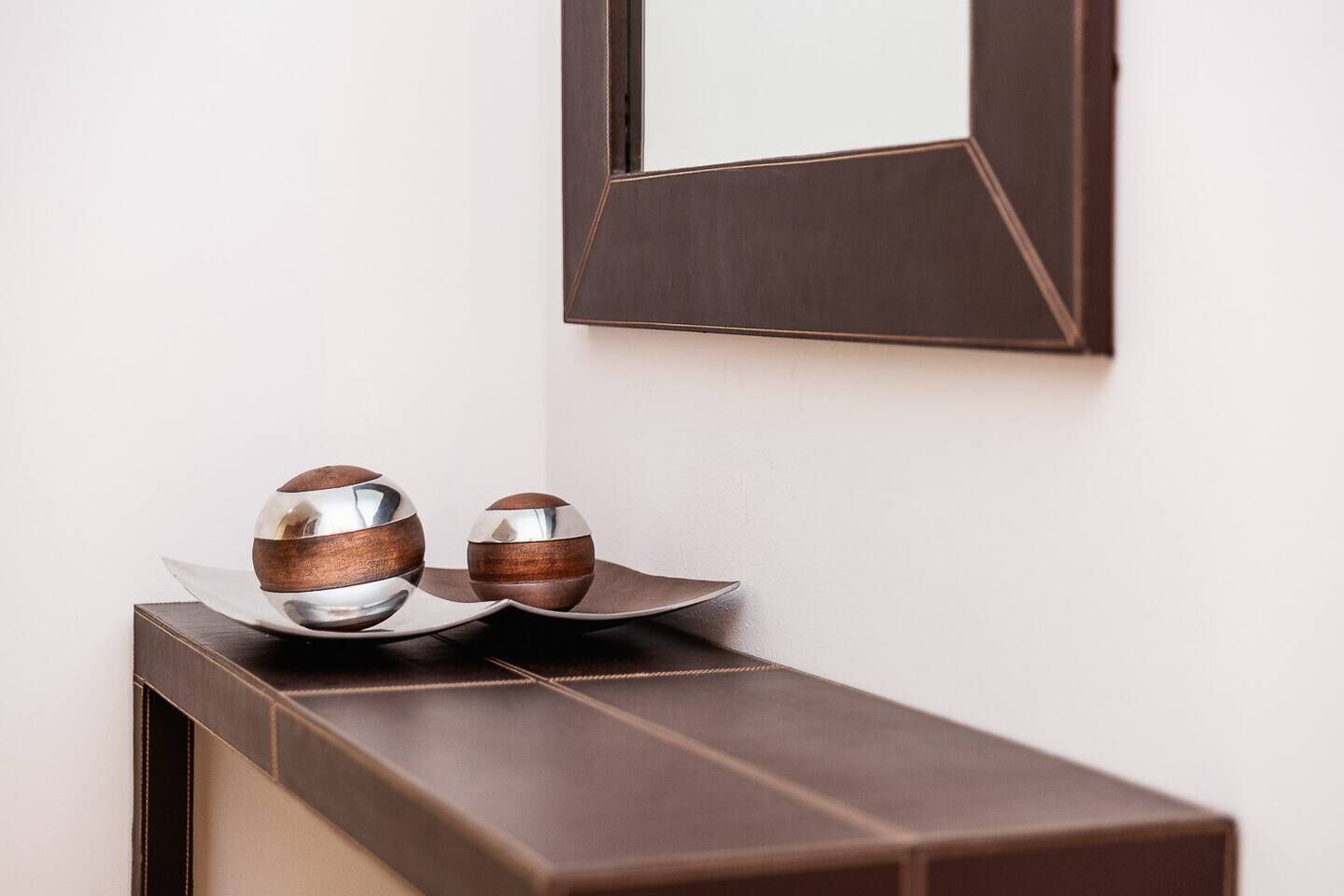 Una consola de madera oscura con dos objetos esféricos de madera y metal encima.