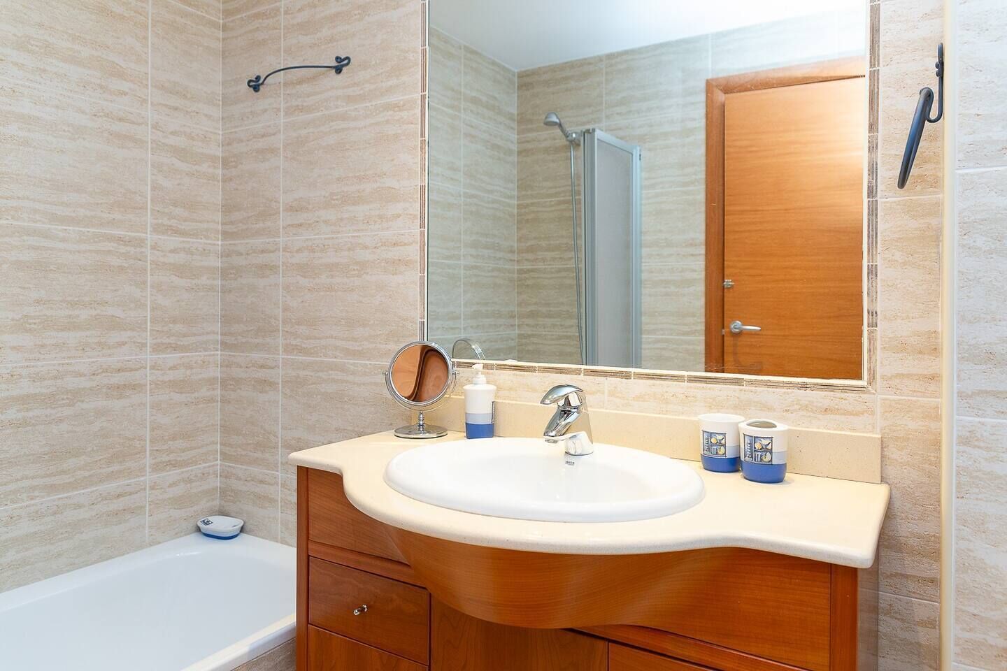 A bathroom with a white sink, wooden vanity, a mirror, and a shower.