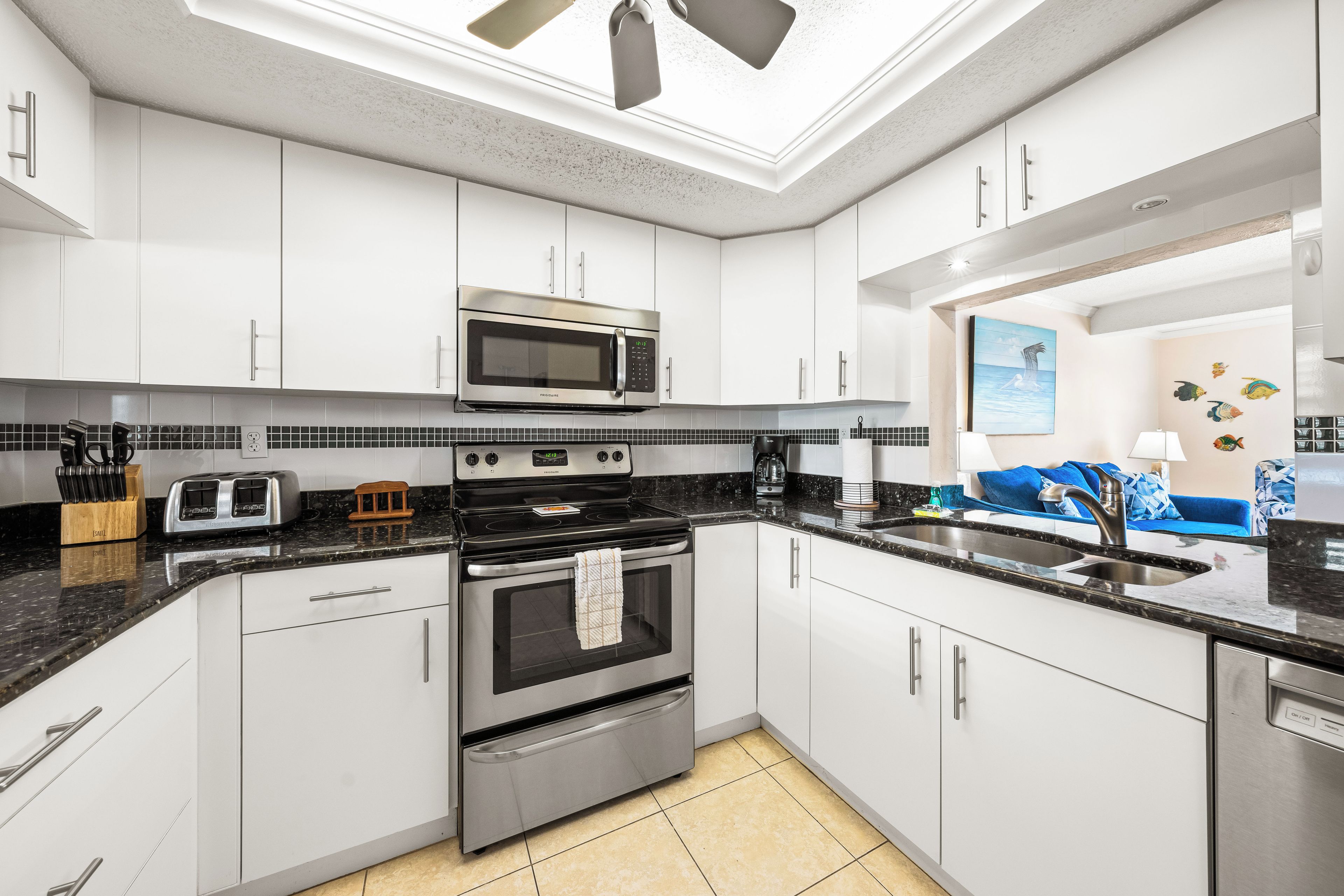 A modern kitchen with white cabinets, a stainless steel microwave, a stove, and a sink.