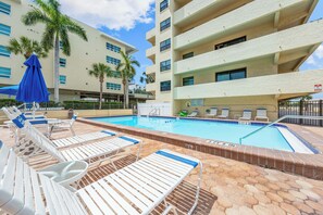 A pool area with lounge chairs and umbrellas, surrounded by a multi-story building with balconies. - Sea Shell by Beachside Management (Siesta Key)