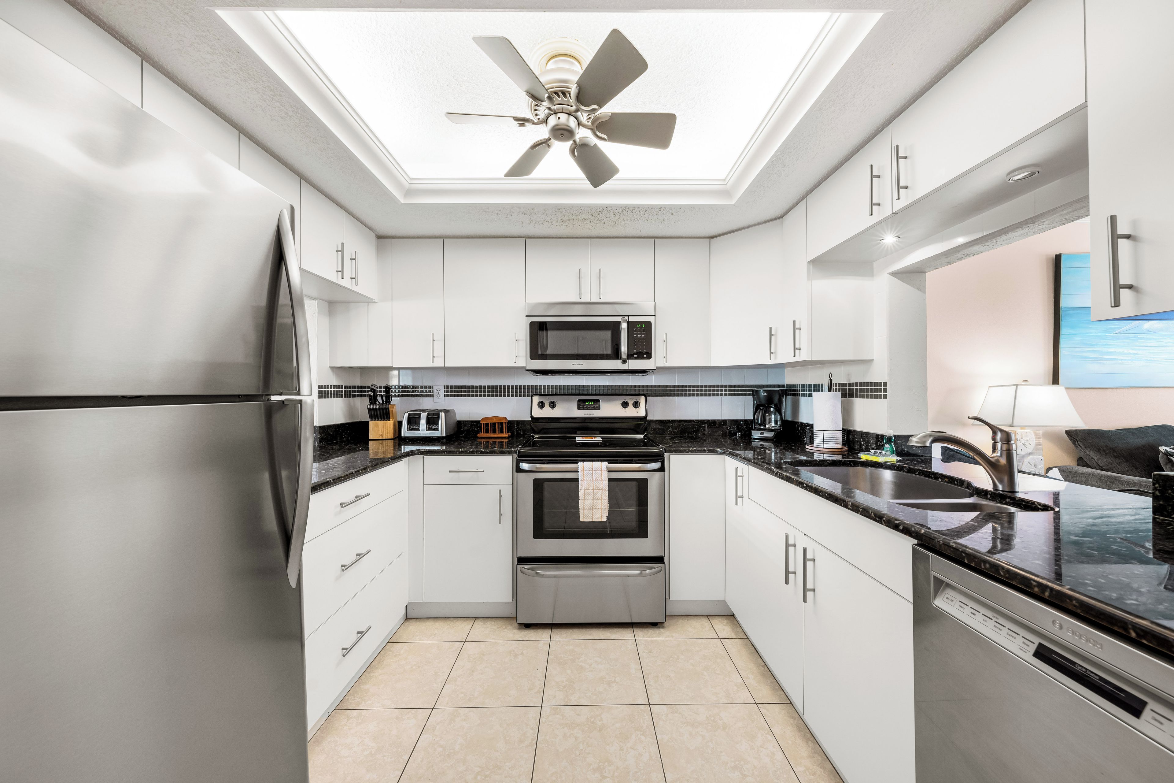Una cocina moderna con electrodomésticos de acero inoxidable, armarios blancos, una encimera negra y un ventilador de techo.