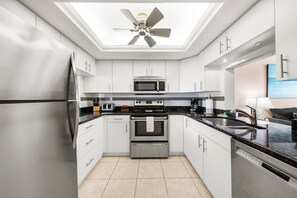 A modern kitchen with stainless steel appliances, white cabinetry, a black countertop, and a ceiling fan.