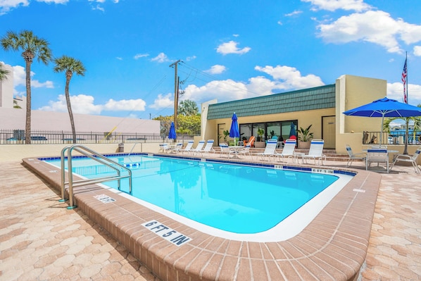 A rectangular swimming pool with a brick edge, surrounded by lounge chairs and umbrellas, under a clear sky. - Sea Shell by Beachside Management (Siesta Key)