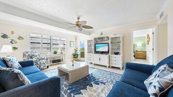 A living room with a television, two sofas, a coffee table, and a ceiling fan.
