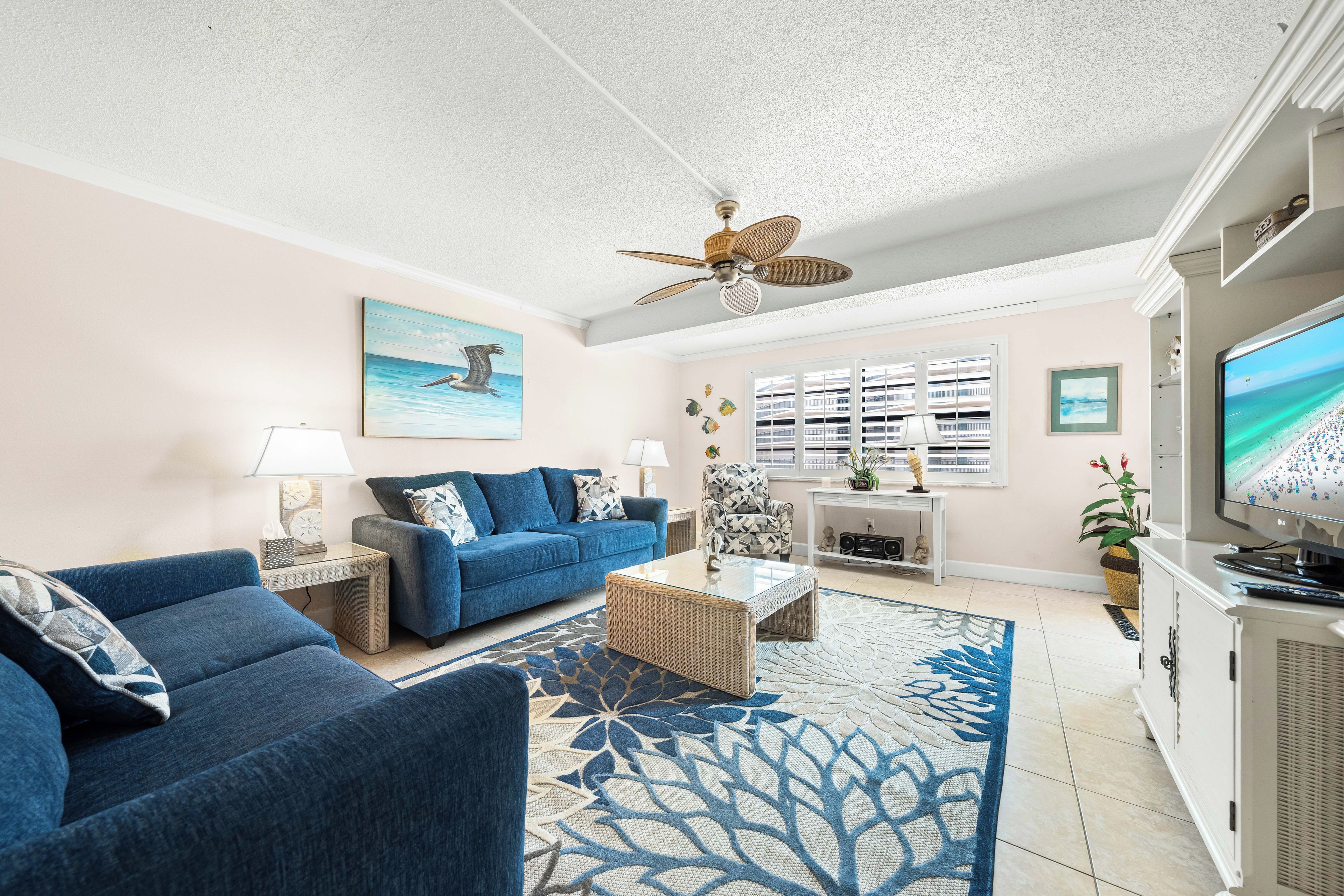 A living room with a blue sofa, a coffee table, a television, and a ceiling fan.