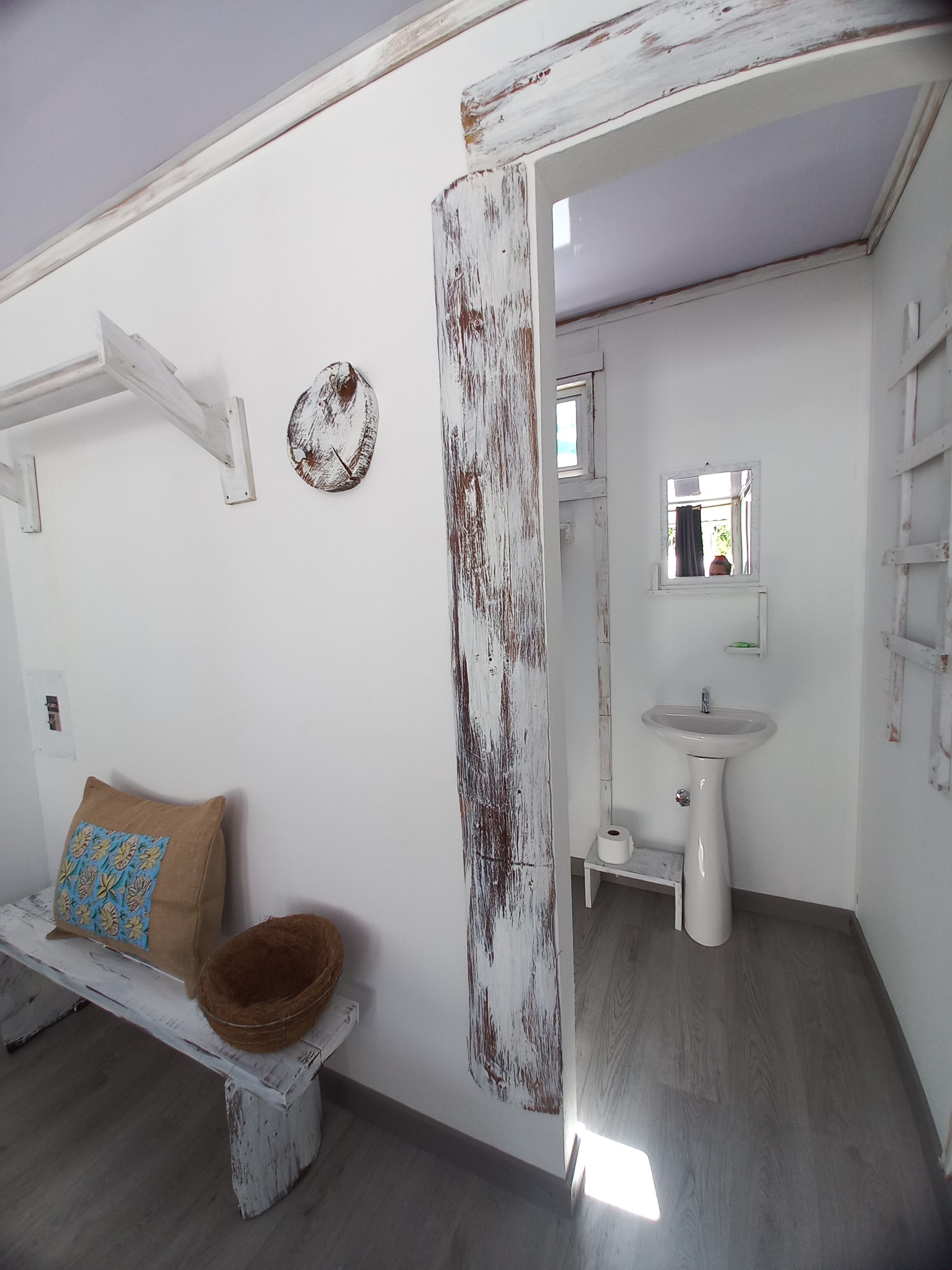 A bathroom with a rustic aesthetic, featuring a white sink, a mirror, and a wooden bench with a bowl.