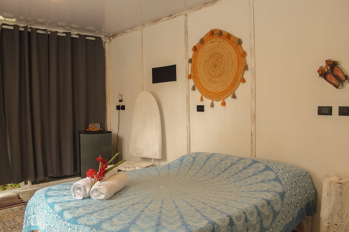 Habitación de hotel con cama, un adorno en la pared, toalla y una pequeña mesa con un florero.
