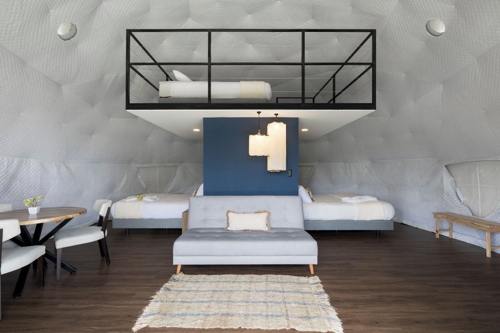 A modern loft bedroom with a mezzanine bed, a sofa, a dining table, and a rug.