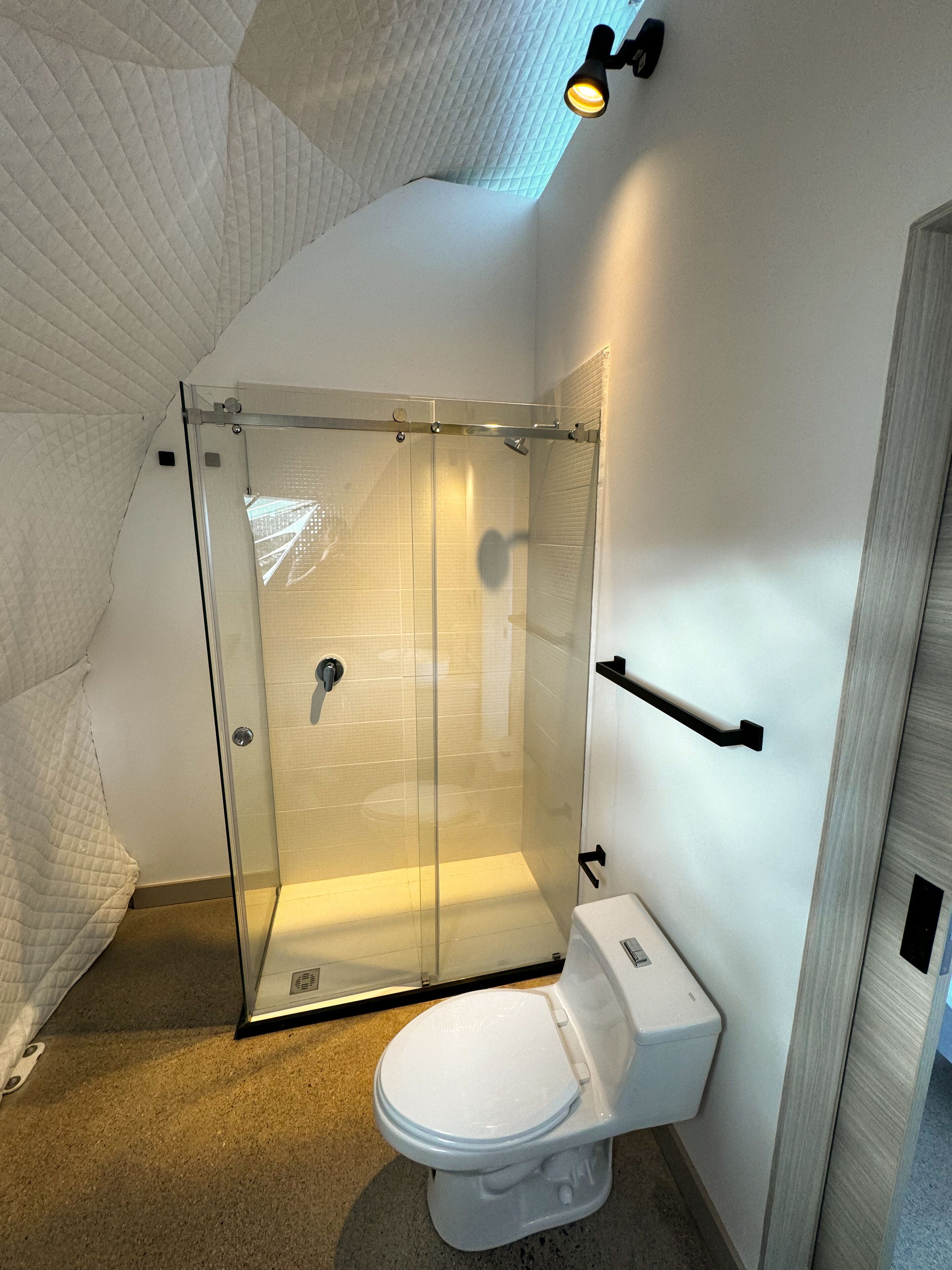 Une salle de bain moderne avec une douche à parois de verre, des toilettes et un porte-serviettes.