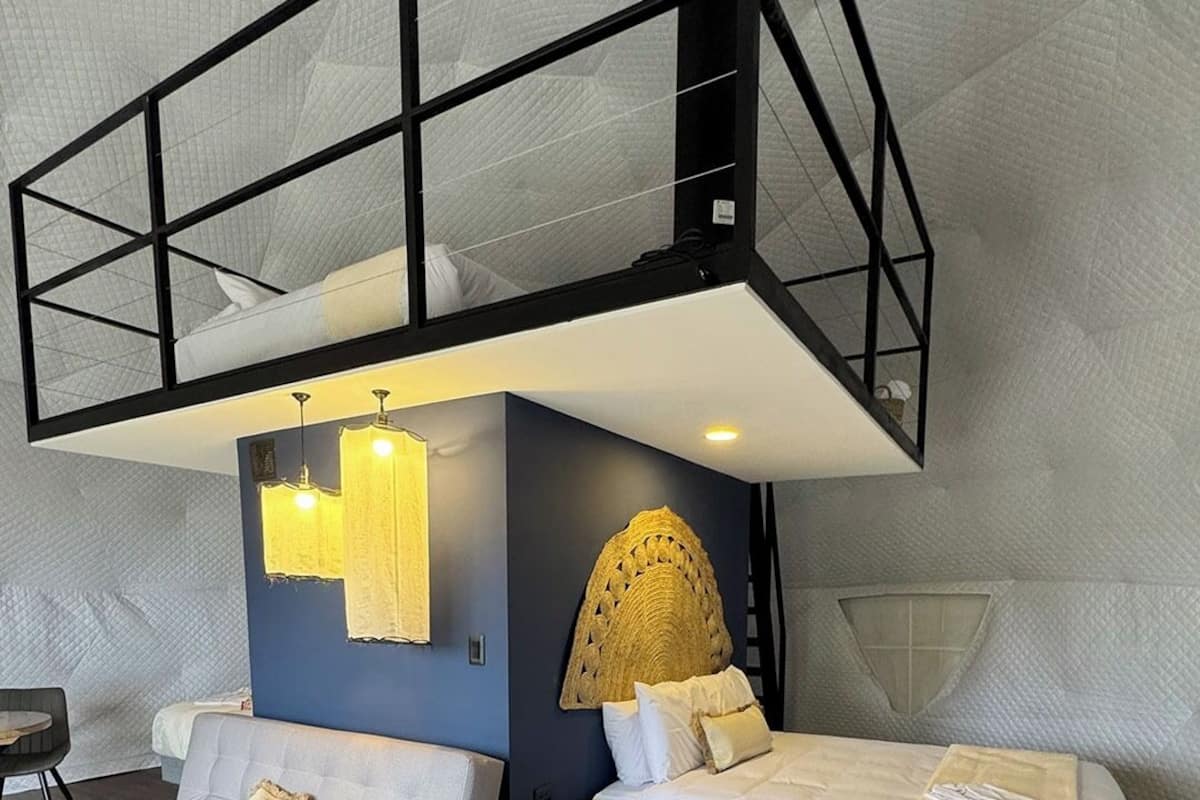 A modern bedroom with a loft bed, a sofa, a bedside table, and a decorative wall piece.