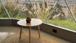 A room with a large window offering a view of a cityscape and mountains. - Naturhotel (Turi)