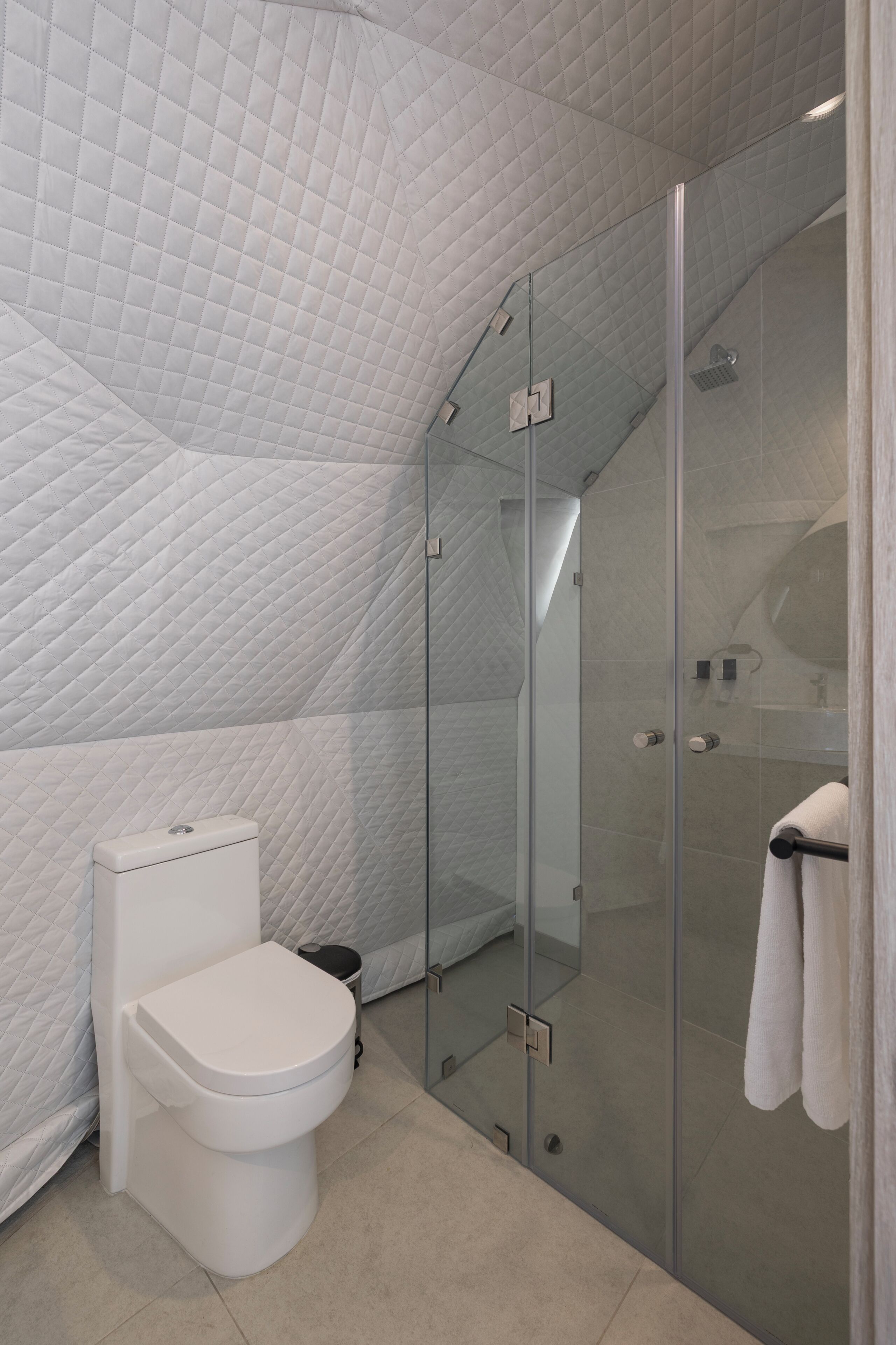Un baño moderno con inodoro blanco, ducha con cerramiento de vidrio y piso de baldosas.