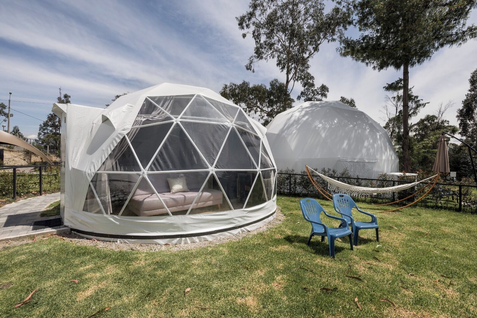 Two geodesic dome structures with transparent walls, one with a visible interior seating area and the other with a hammock and chairs outside.