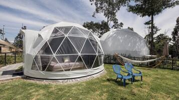 Two geodesic dome structures with transparent walls, one with a visible interior seating area and the other with a hammock and chairs outside.