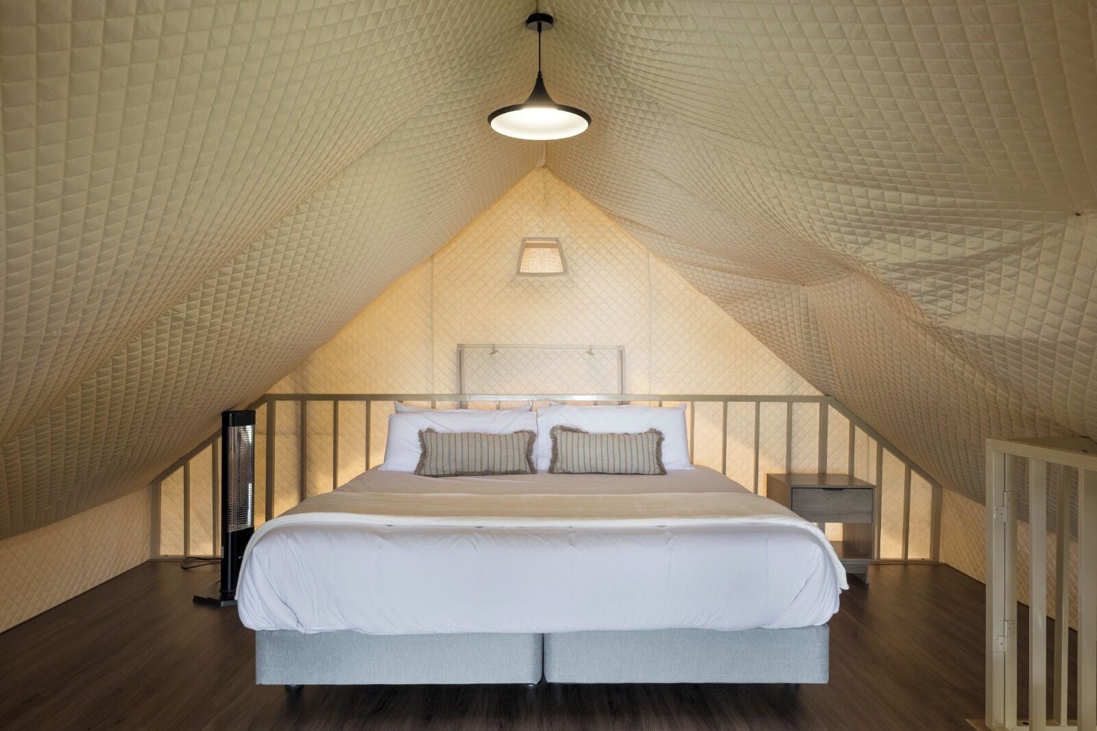 A bedroom with a sloped ceiling, a bed with white linens, a bedside table, and a hanging light fixture.