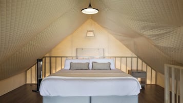 A bedroom with a sloped ceiling, a bed with white linens, a bedside table, and a hanging light fixture.