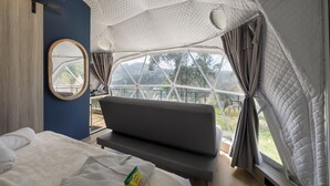 A room with a bed, a bench, a round mirror, and a view through a large window. - Naturhotel (Turi)
