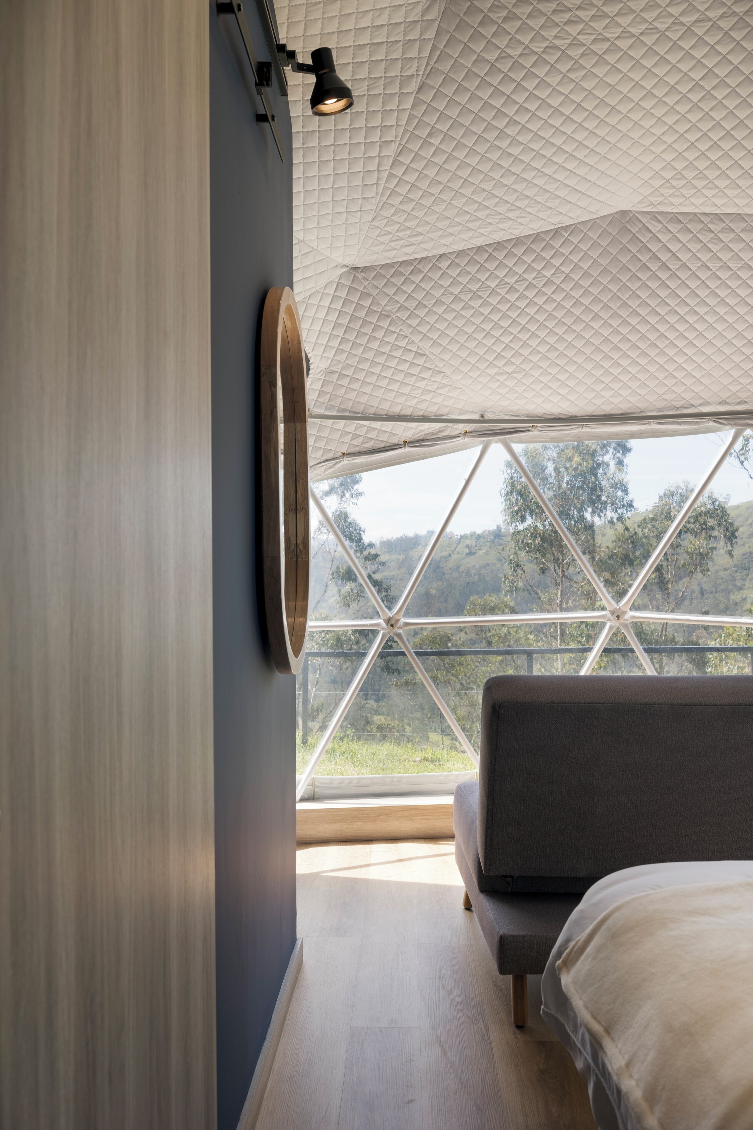A bedroom with a large window, a bed, and a wall-mounted light fixture.