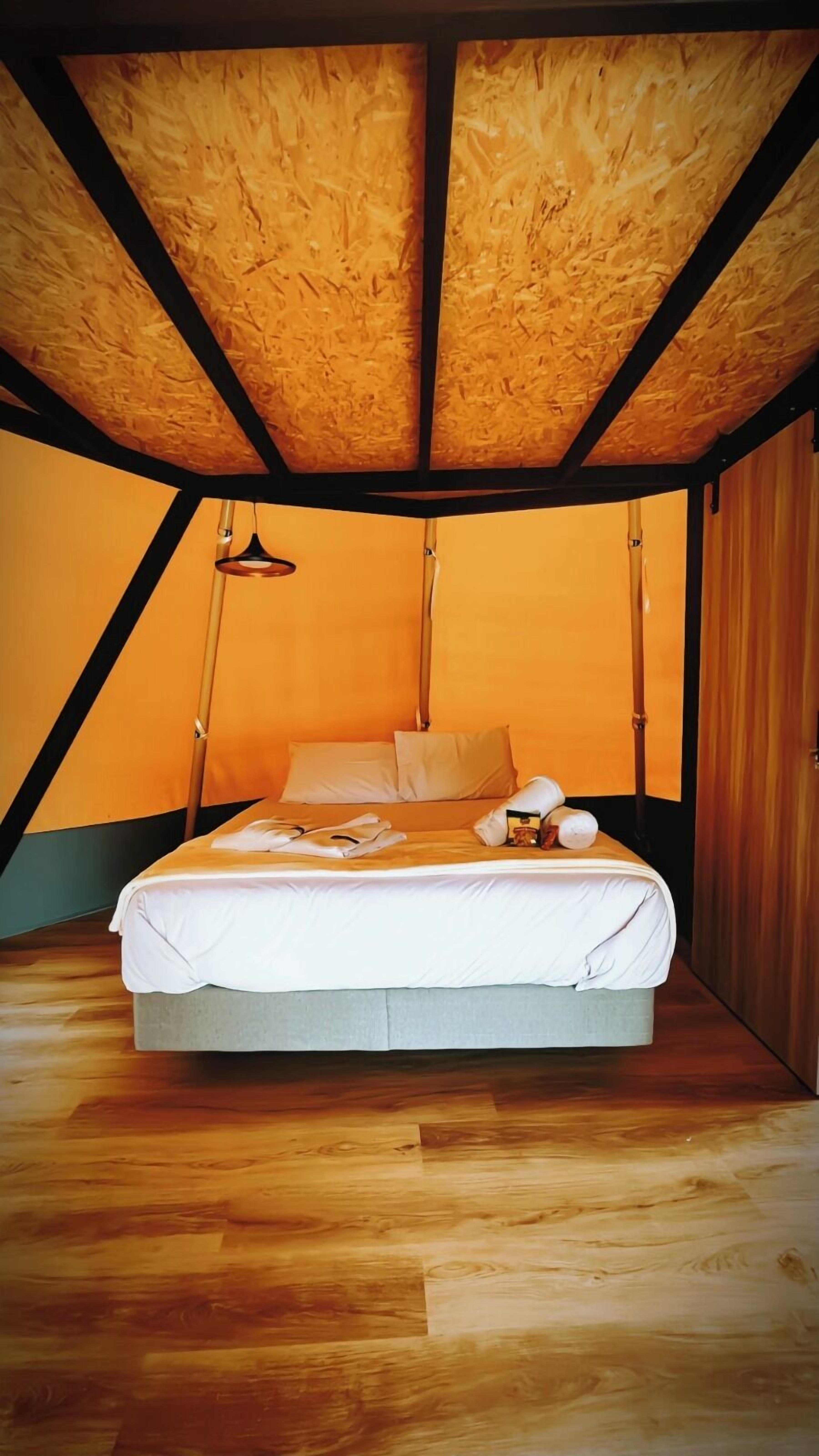 A triangular room with a bed, wooden beams, and a slanted ceiling.