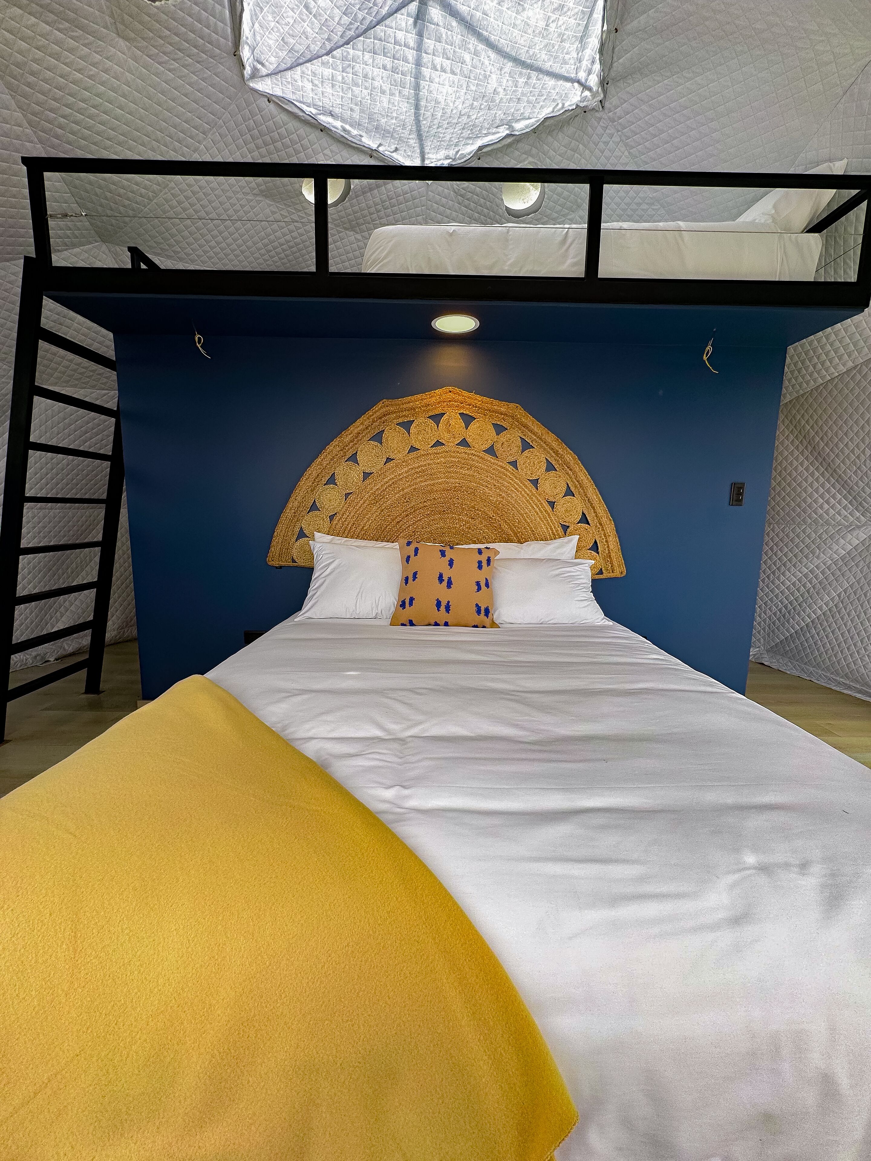 Una cama litera con cabecera azul y manta amarilla.