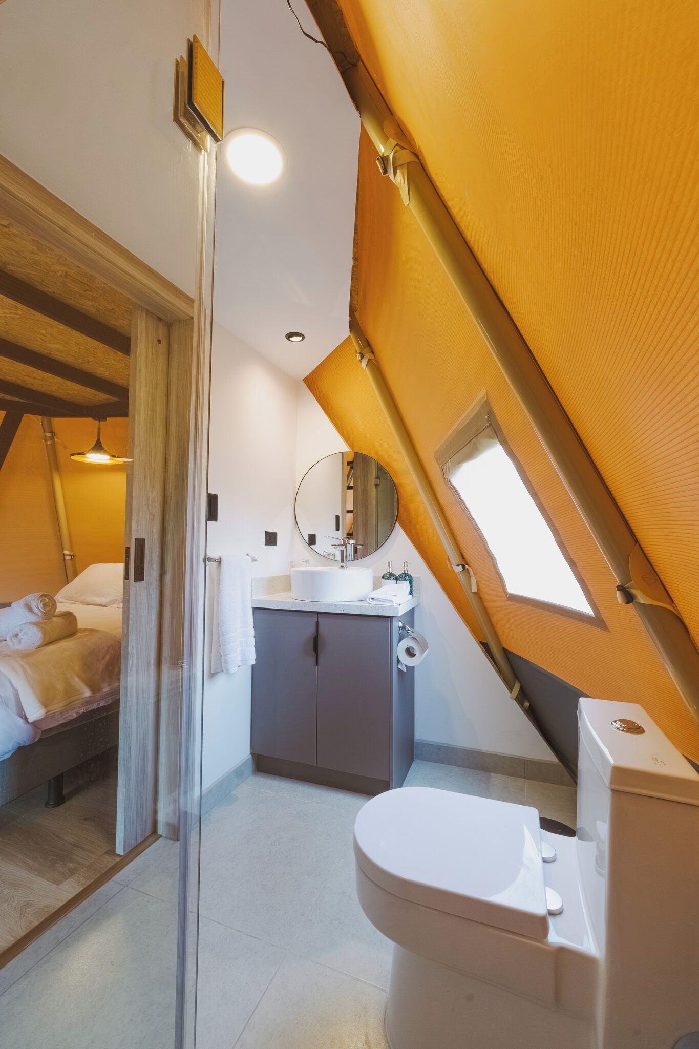 Un dormitorio con cama, un baño con inodoro y un tragaluz.