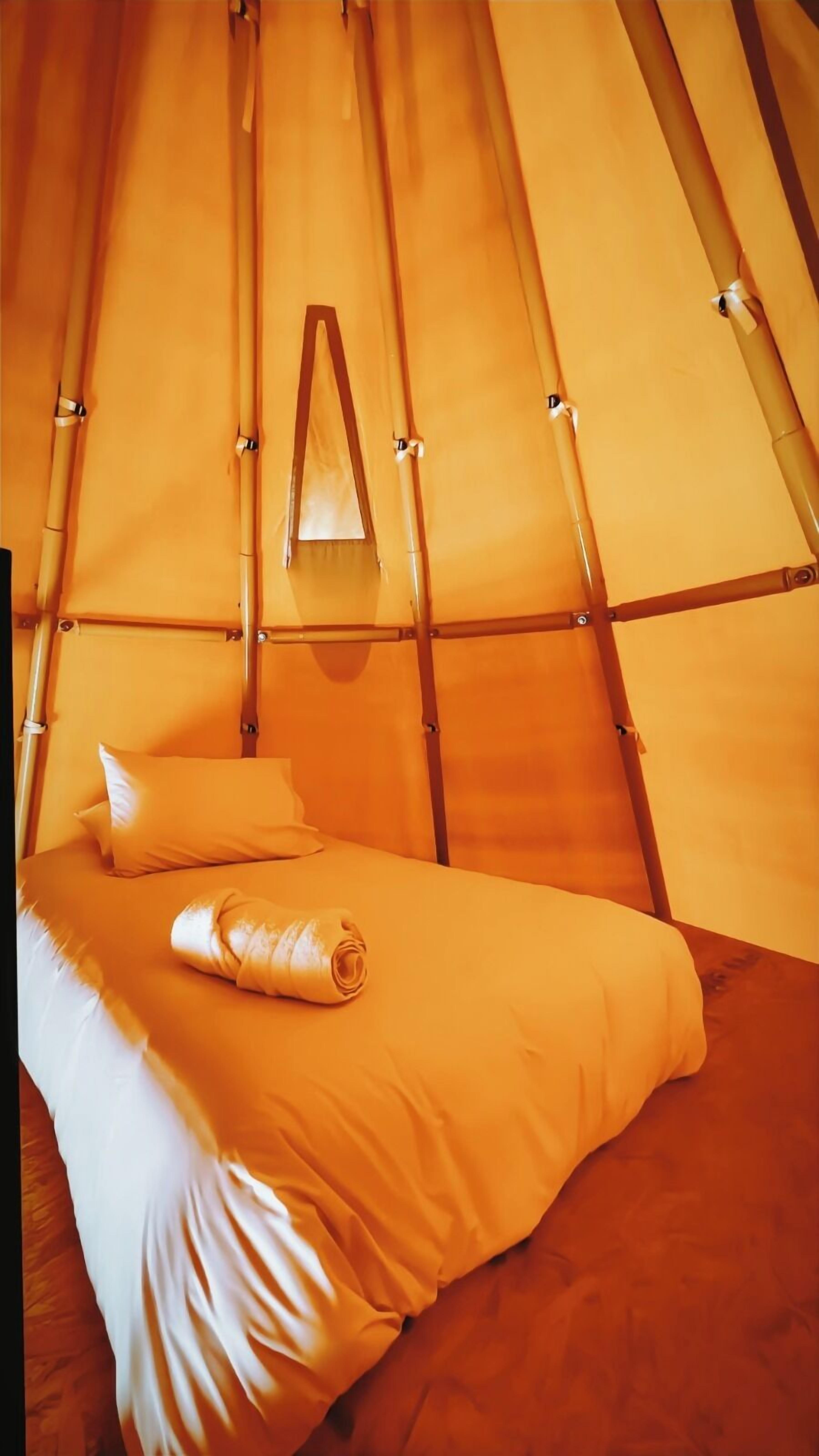 Uma cama de solteiro com um cobertor enrolado em uma estrutura tipo tenda com estrutura de bambu.