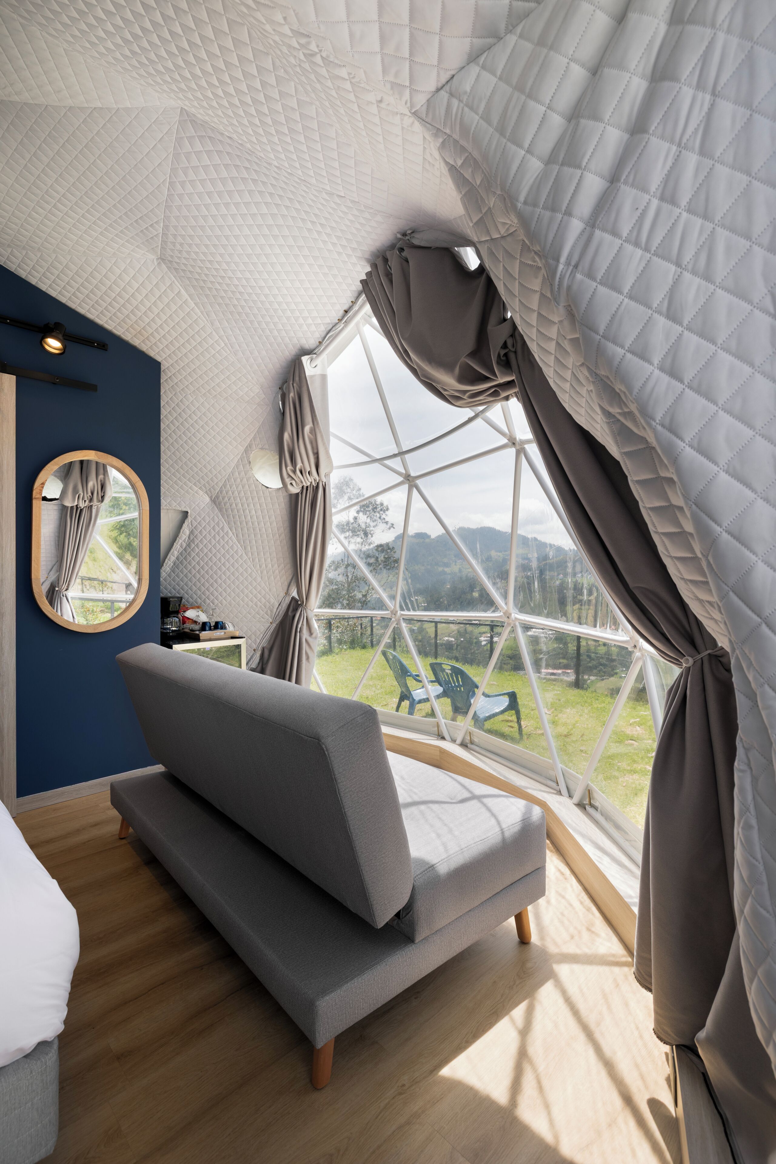 A cozy room with a large window, a sofa, a mirror, and a wooden floor.