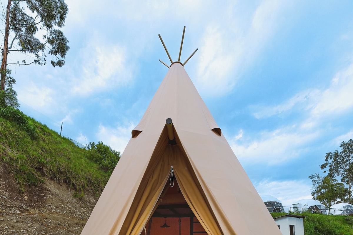 A teepee-style tent with a bed inside, set on a concrete base with a grassy area around.