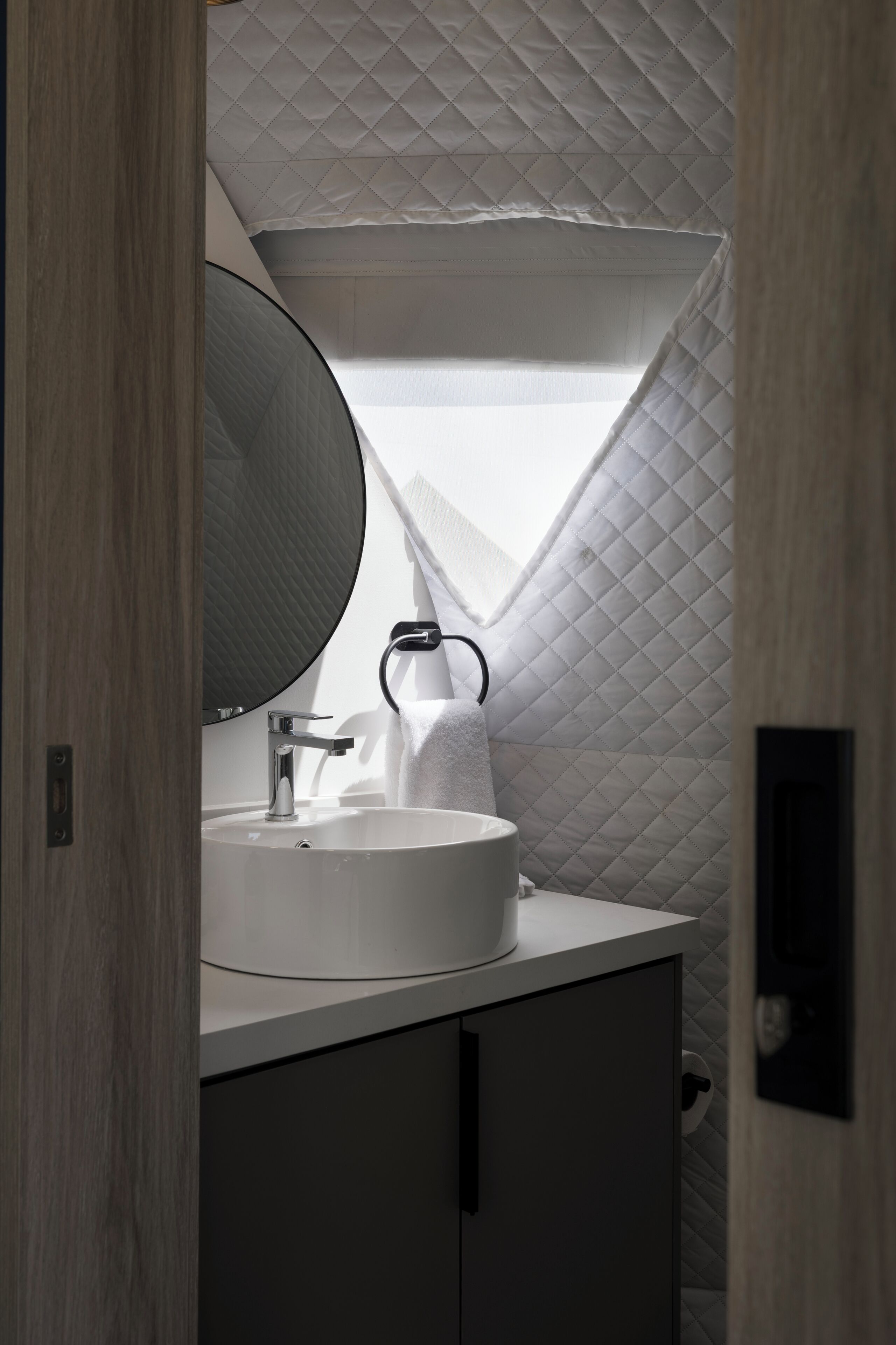 A bathroom with a round mirror, a white sink, and a towel dispenser.
