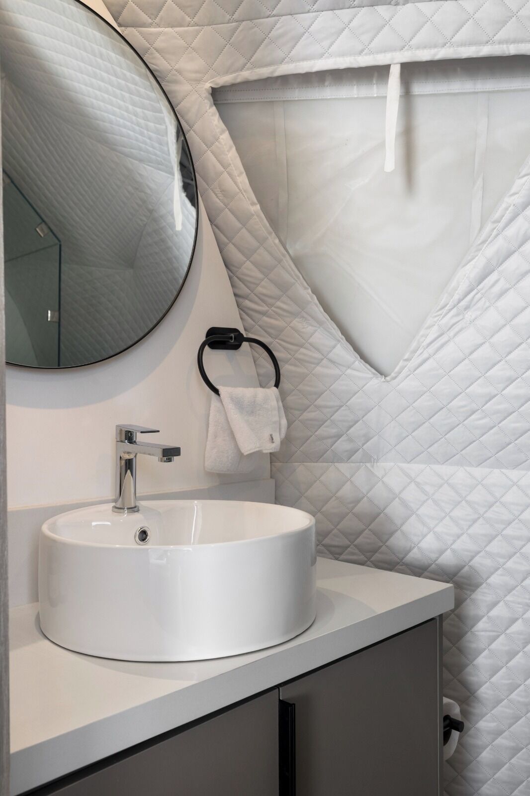Un baño moderno con un espejo redondo, un lavamanos blanco y un diseño de pared acolchado.