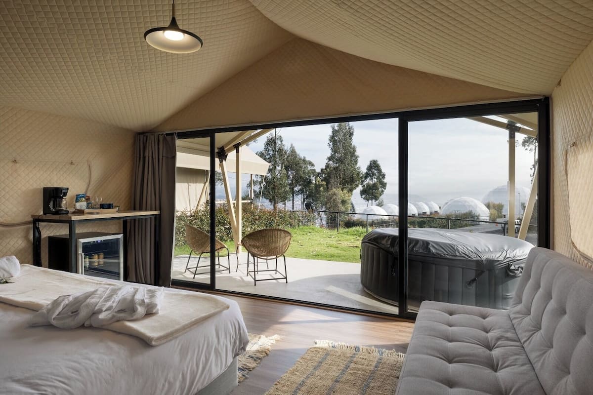 A modern bedroom with a large bed, a sofa, and a hot tub.