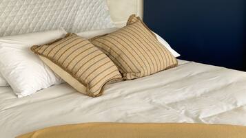 Una cama con ropa de cama blanca, dos almohadas a rayas y una manta beige.