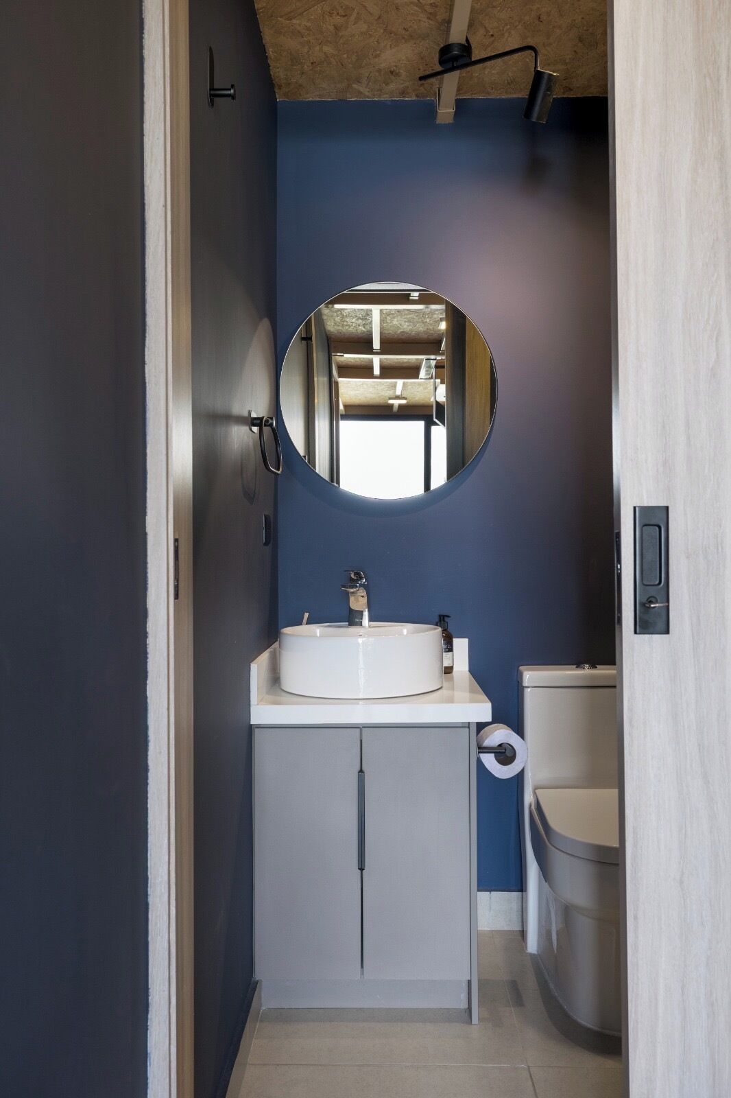 A bathroom with a round mirror, a white sink, and a toilet.