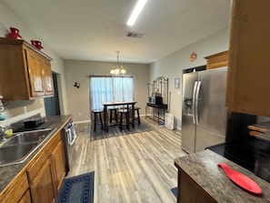 A kitchen with wooden cabinets, a dining table with stools, a refrigerator, and a microwave.