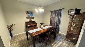 A dining room with a wooden table, chairs, a chandelier, a piano, and a cabinet.