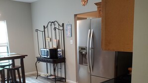 A kitchen with a stainless steel refrigerator, a microwave, and a gas stove. There is a wooden table and chairs, and a small cabinet with a fire extinguisher.