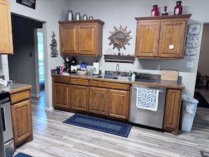 A kitchen with wooden cabinets, a stainless steel sink, and a blue rug.