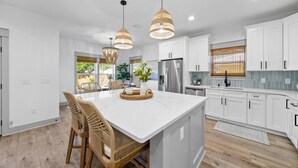 Una cocina moderna con armarios blancos, una isla grande con asientos y dos lámparas colgantes.