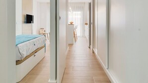 Ein heller, moderner Flur mit Holzboden, der zu einem Schlafzimmer mit Bett und Wandfernseher führt.