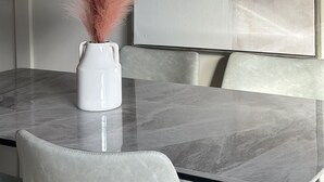 Ein Esstisch mit einer weißen Vase, gefüllt mit rosa Pampasgras, ein grauer Stuhl und ein großes gerahmtes abstraktes Gemälde an der Wand.