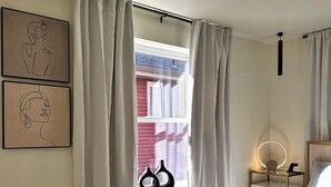 Ein Schlafzimmer mit einem Bett, einem Nachttisch mit Lampe und einem Fenster mit Vorhängen.