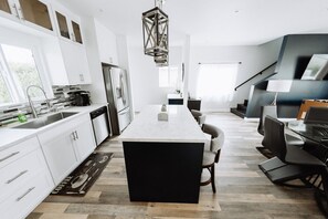 A modern kitchen with white cabinetry, a central island, a dining area with black chairs, and a staircase. - ELEGANT, MODERN, WELL-APPOINTED 3BR HOME with PRIVATE HOT TUB,  BUILT IN 2020 (p26) (Los Angeles)