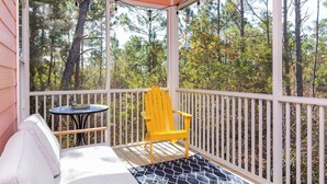 A covered porch with a white railing, a yellow Adirondack chair, a small round table, and a blue patterned rug. - Cute Cottage~2 Pools~Beach Nearby ~ Book Now for a Relaxing Stay! (Gulf Shores)