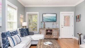 A living room with a gray sofa, wooden coffee table, and a TV on the wall. - Cute Cottage~2 Pools~Beach Nearby ~ Book Now for a Relaxing Stay! (Gulf Shores)