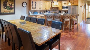 Un coin repas avec une table et des chaises en bois, une cuisine avec des meubles et des appareils électroménagers en bois, et une horloge au mur.