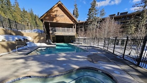 A pool area with a hot tub, surrounded by a wooden lodge and a fenced deck.