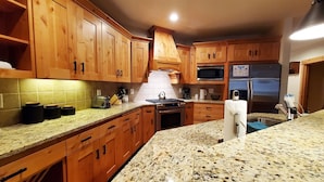 A kitchen with wooden cabinets, granite countertops, a stove, microwave, and refrigerator.