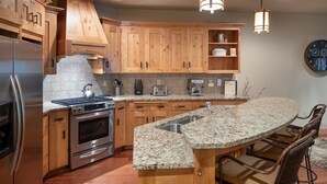 Una cocina moderna con armarios de madera, encimera de granito, electrodomésticos de acero inoxidable y una zona de bar con taburetes.