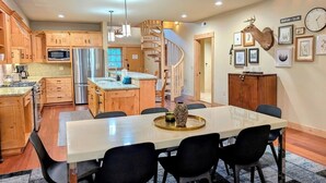 A modern kitchen with wooden cabinets, a central island, and a dining area with a large table and chairs.
